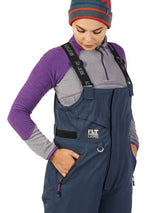 Woman wearing navy blue FLT Light ice fishing bibs with purple fleece layer, ideal for cold weather outdoor gear