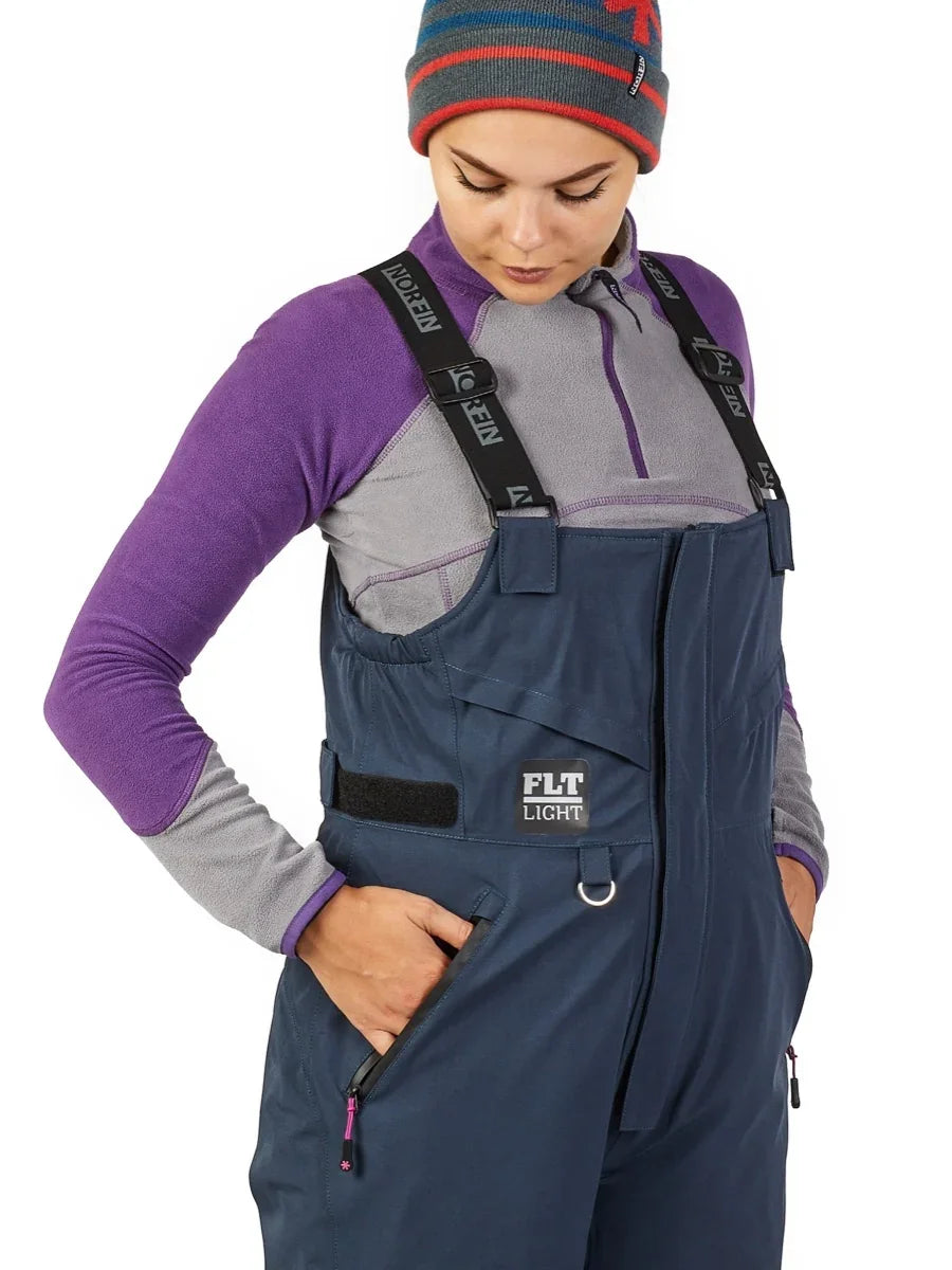 Woman wearing navy blue FLT Light ice fishing bibs with purple fleece layer, ideal for cold weather outdoor gear